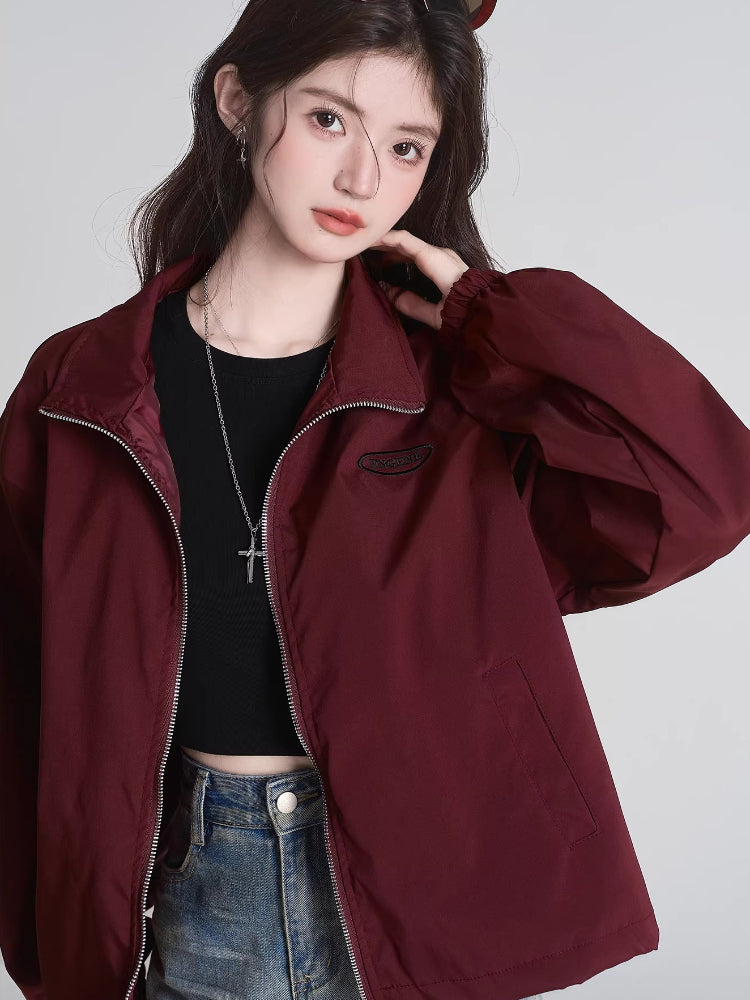 Close-up of a woman's face and upper body wearing a maroon bomber jacket