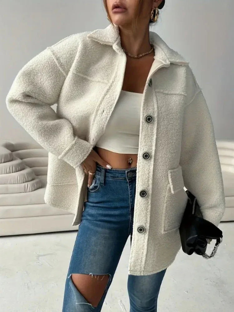 Woman wearing an oversized white sherpa fleece jacket over a white crop top and ripped blue jeans. Main image