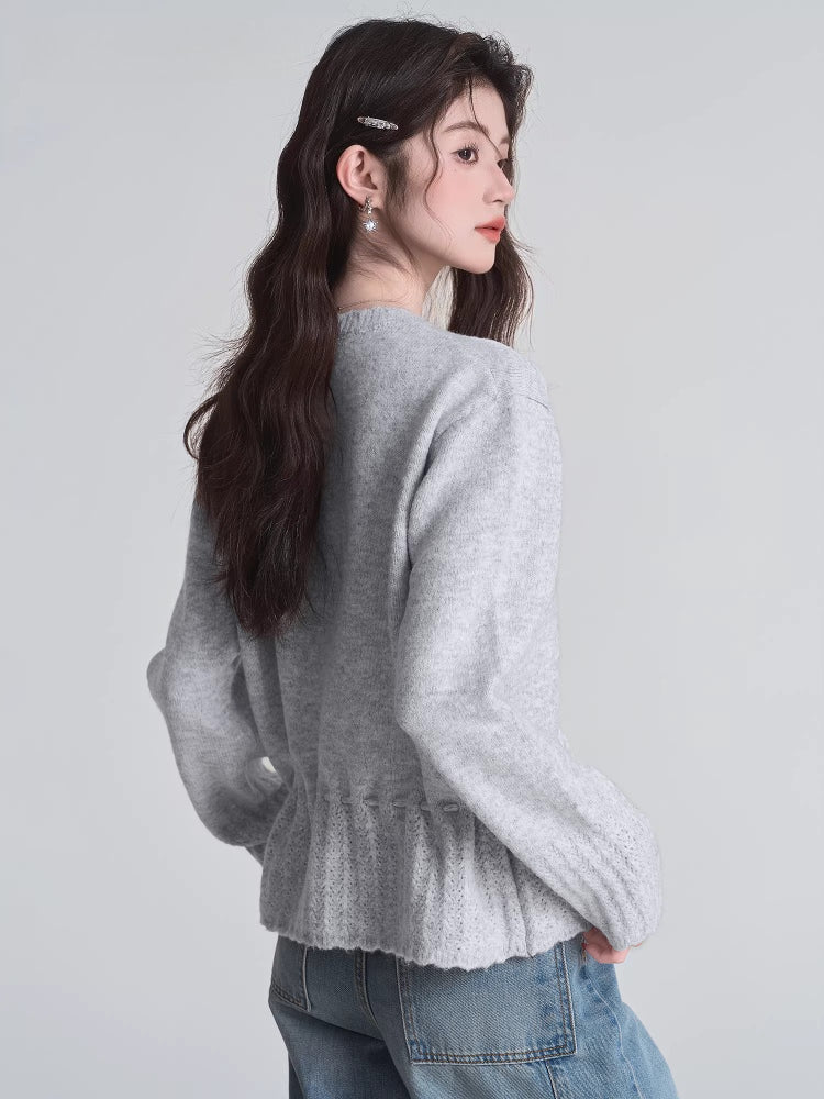 Rear view of a woman wearing a light grey knit cardigan with a drawstring waist and button front closure, paired with blue jeans.