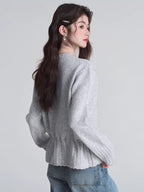 Rear view of a woman wearing a light grey knit cardigan with a drawstring waist and button front closure, paired with blue jeans.