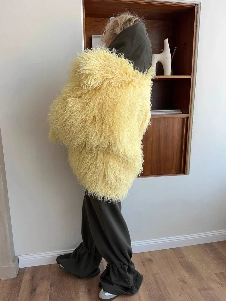 Woman wearing a yellow shaggy faux fur jacket over a dark green hooded sweatshirt with dark green pants.