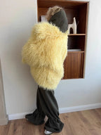 Woman wearing a yellow shaggy faux fur jacket over a dark green hooded sweatshirt with dark green pants.