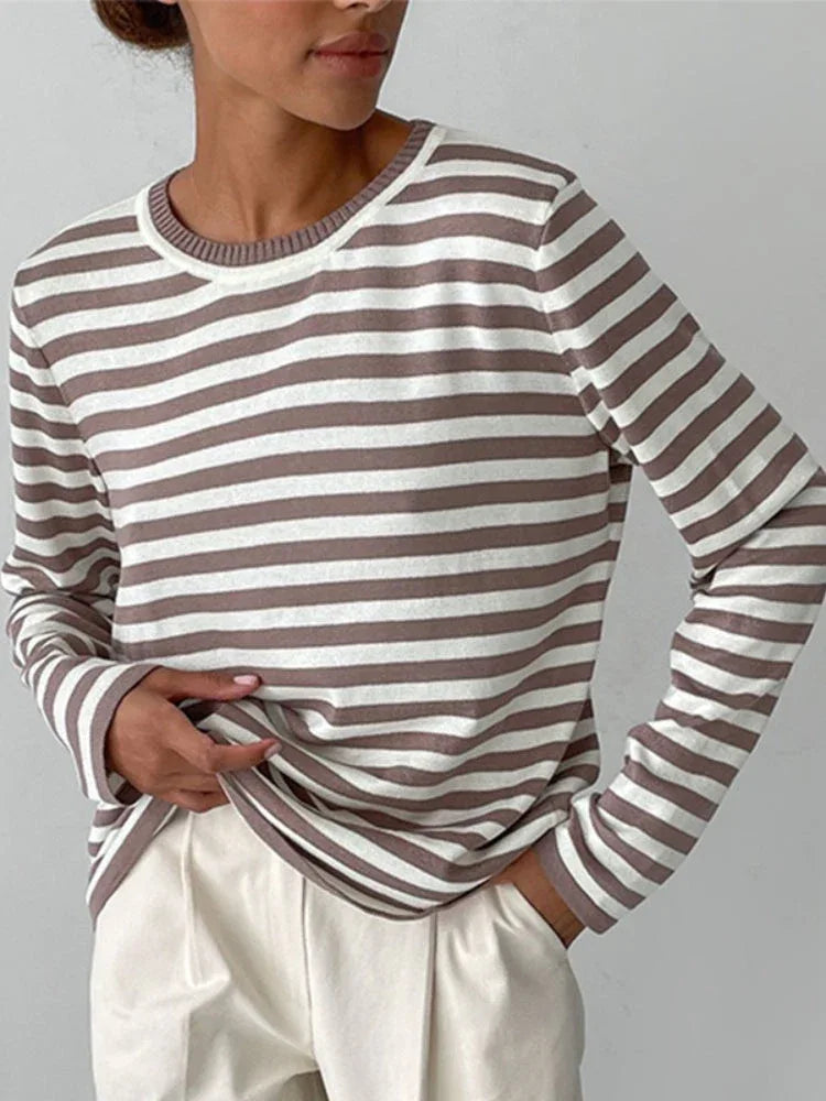 Woman wearing a brown and white striped long-sleeved crew neck sweater with cream-colored pants, hands tucked into her pockets. Main image
