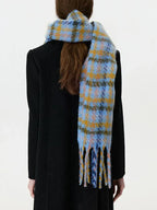 Back view of a woman wearing a black coat and a blue and yellow plaid scarf with fringe