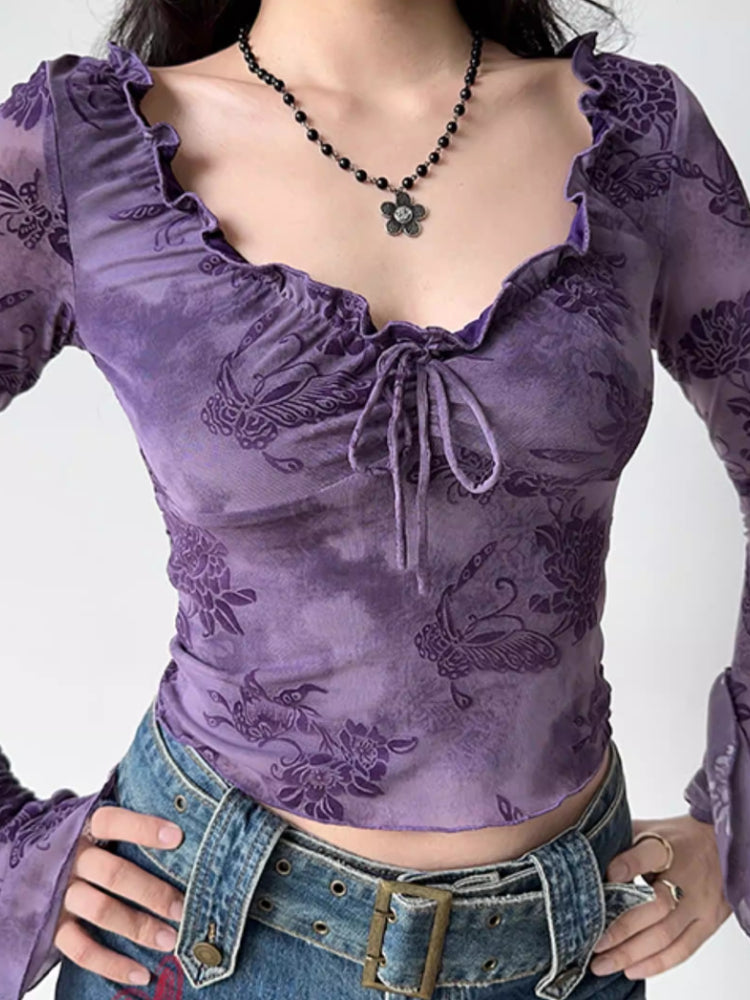 Front view of a woman wearing a purple sheer mesh top with a floral print and a tie-front closure.