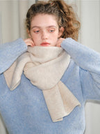 Model adjusting a light blue knit sweater and a cream scarf.