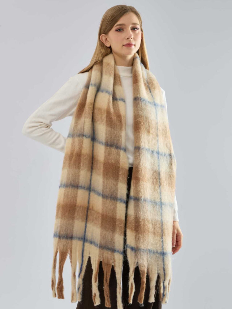 A woman stands facing forward, showcasing a large, plaid, fuzzy knit scarf with fringe.