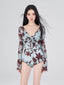 Woman wearing a light blue one-piece swimsuit with a brown floral print and long sheer sleeves, front view.