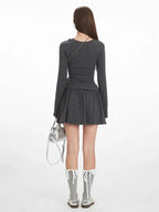 Back view of a woman wearing a dark grey long-sleeve mini dress with a gathered waist, white-trimmed grey socks, and silver shoes, holding a silver handbag.