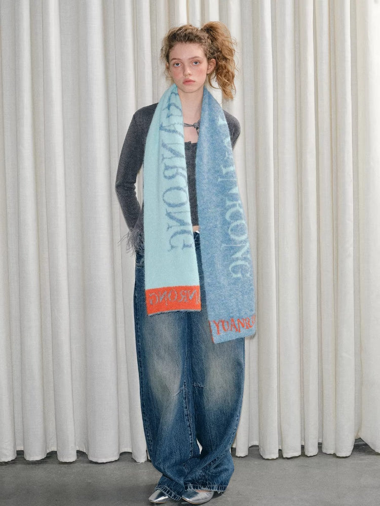 Model wearing a gray long-sleeved top, blue jeans, and a scarf.