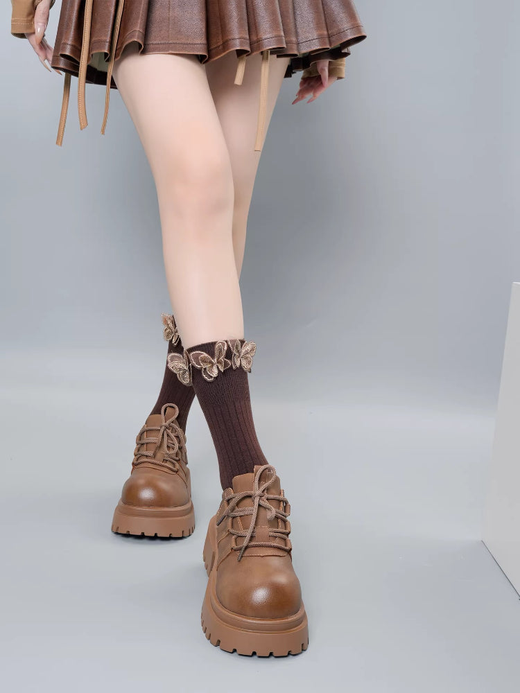 Front view of brown ribbed socks with ruffled butterfly trim and brown lace-up platform shoes, worn with a brown skirt.