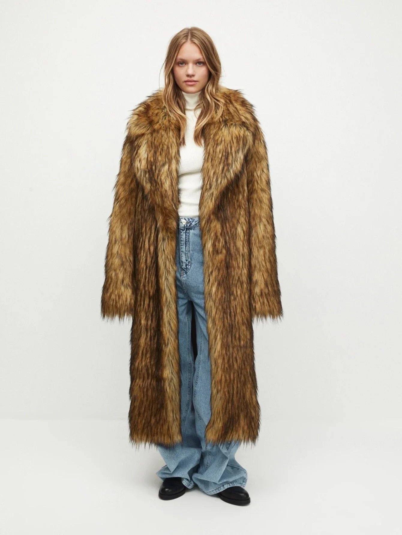 Woman wearing a long brown faux fur coat with a white turtleneck and blue jeans, front view. Main image