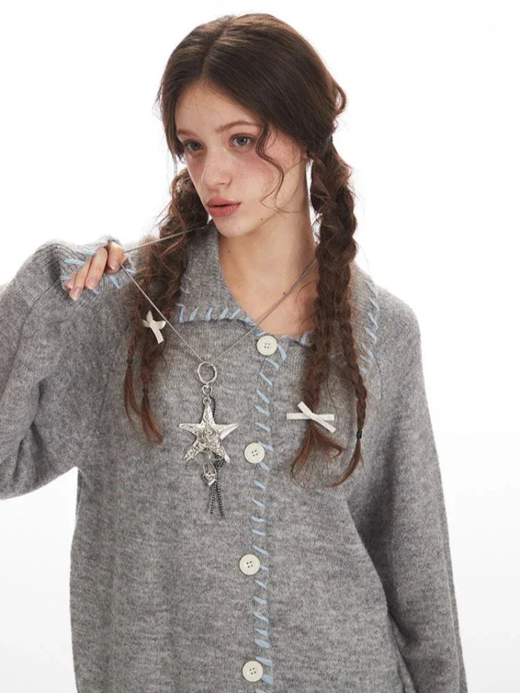 Close-up of a model wearing a grey knitted cardigan, focusing on the necklace and hair accessories.