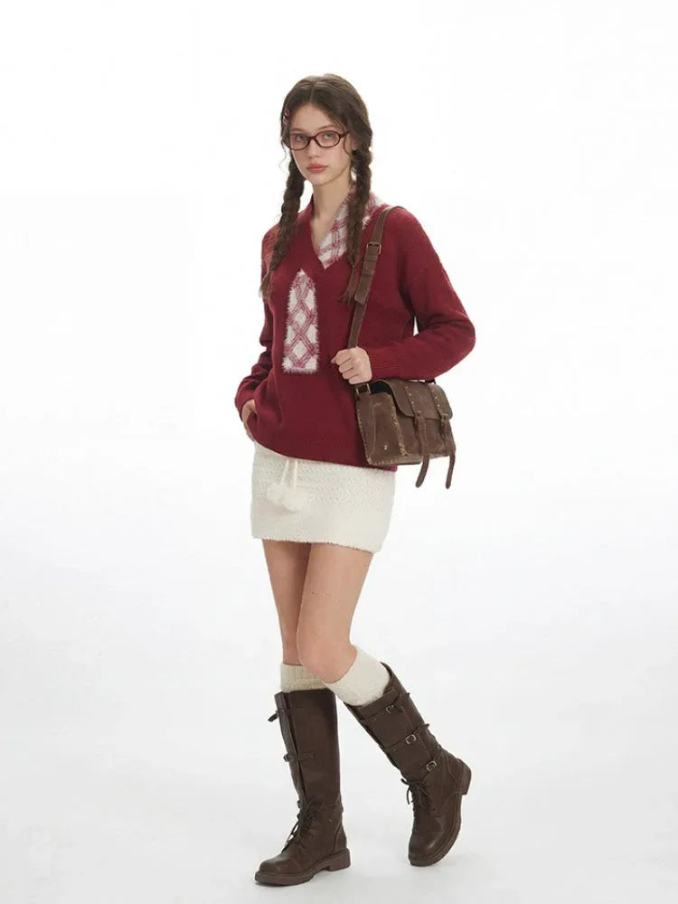 Woman poses with one leg forward, wearing a burgundy v-neck sweater with a white plaid detail, a white textured mini skirt, white knee-high socks, and brown buckled boots, carrying a brown crossbody bag.