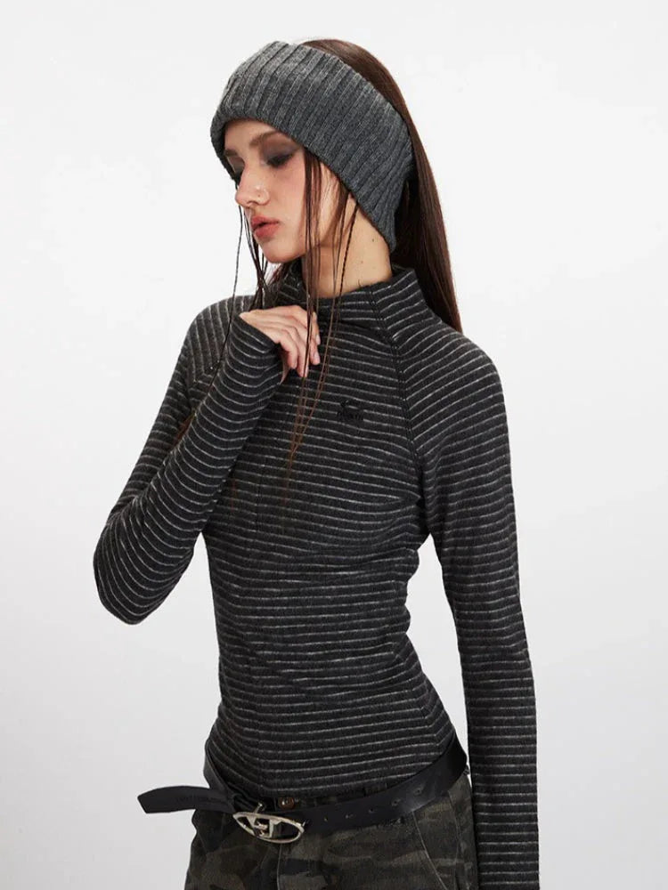 Close-up profile view of a model wearing a gray striped long-sleeve top with a mock neck and thumbholes, paired with camouflage cargo pants and a black belt.