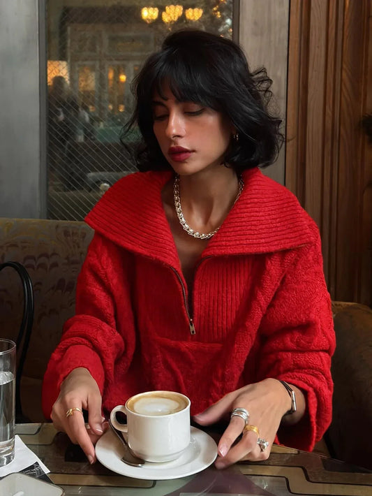 Woman wearing a red textured knit quarter zip sweater with black pants and silver jewelry, holding a coffee cup.