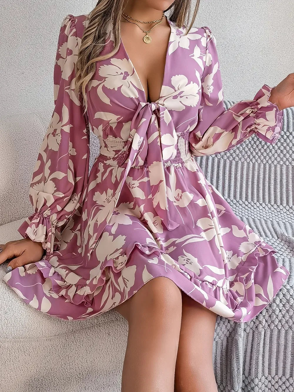 woman sitting on a couch wearing a purple floral print mini dress with a tie front