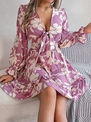 woman sitting on a couch wearing a purple floral print mini dress with a tie front