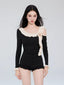 Woman wearing a black one-piece swimsuit with an off-the-shoulder neckline and ruffle trim.