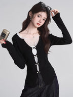 Woman wearing a black long-sleeved top with white lace trim and decorative buttons, holding a vintage camera.
