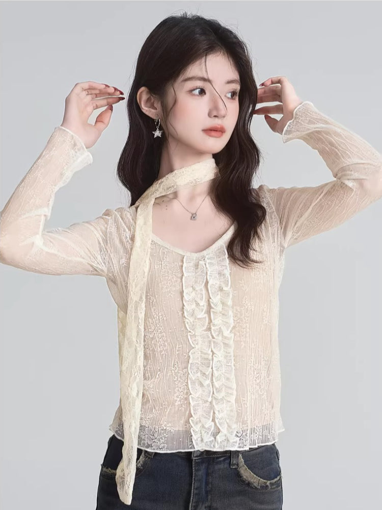 Close-up of a woman's face and upper body wearing a cream lace top with a scarf detail and star earrings.