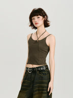 Woman wearing a dark olive green halter crop top with a ring detail at the neckline and a dark wash wide-leg jean with a grommet belt, full body shot.