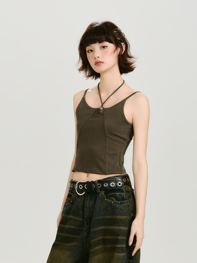 Woman wearing a dark olive green halter crop top with a ring detail at the neckline and a dark wash wide-leg jean with a grommet belt, full body shot.