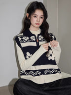 Close-up of a woman wearing a navy and cream floral and geometric knit vest over a cream long-sleeve top and dark wash wide-leg jeans, adjusting the zipper.