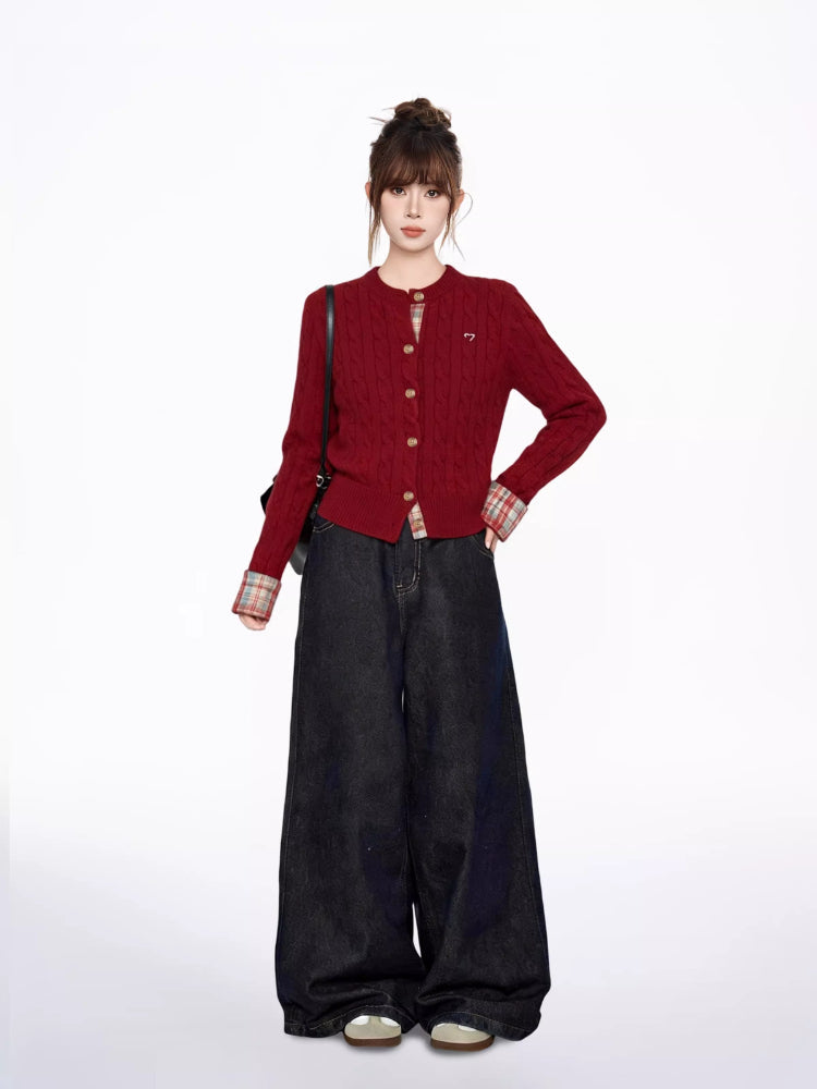 Woman standing with a black shoulder bag, wearing a red cable knit cardigan over a plaid shirt and dark wash wide-leg jeans.