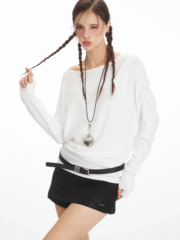 Model wearing a white off-the-shoulder long-sleeve top, black high-waisted shorts, black belt, and black knee-high socks, winking and holding her braided hair.