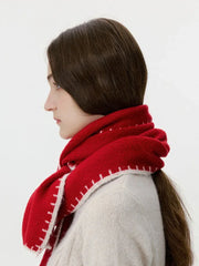 Woman wearing a red knit scarf with white contrast stitching over a cream cable knit sweater, profile view looking right.
