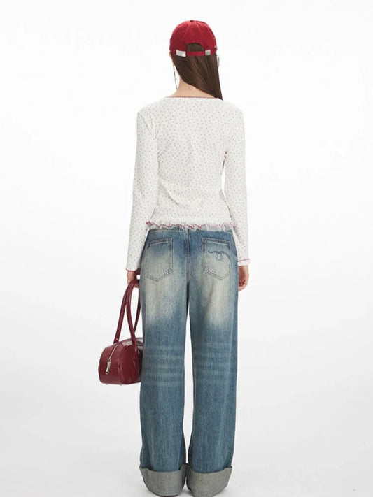 Back view of a model wearing a white long-sleeve top with a floral print and red trim, paired with blue jeans and a red handbag.