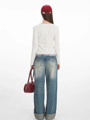 Back view of a model wearing a white long-sleeve top with a floral print and red trim, paired with blue jeans and a red handbag.