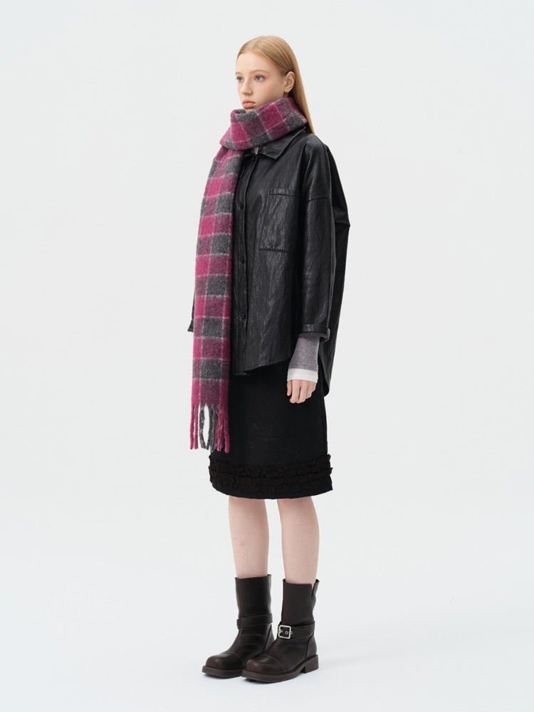 Side view of a woman wearing a black leather-look jacket, a black skirt with ruffled hem, a pink and grey plaid scarf, and black boots.