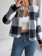 Woman wearing a cropped buffalo plaid jacket over a white tank top and blue jeans, with a black belt, touching her necklace.