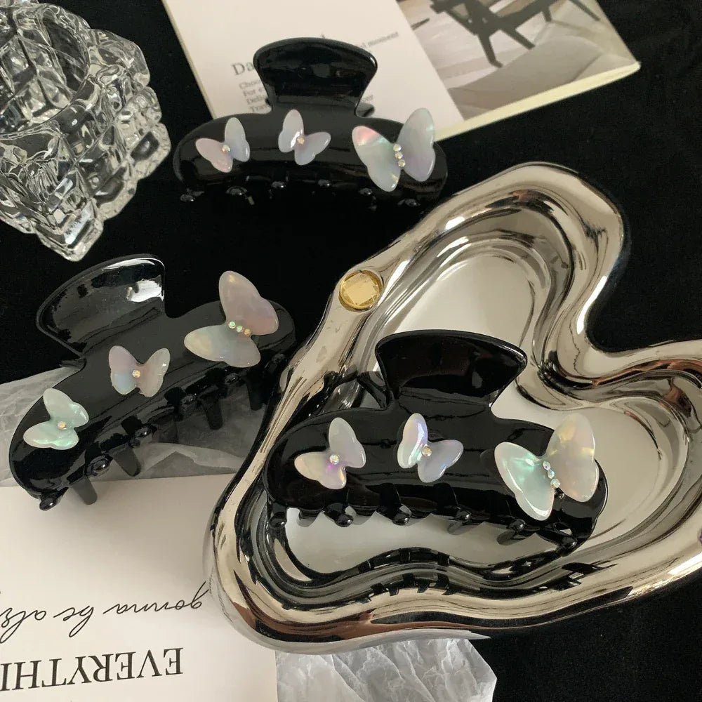 Collection of black claw clips with iridescent butterfly embellishments displayed on a silver heart-shaped tray