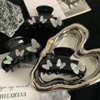 Collection of black claw clips with iridescent butterfly embellishments displayed on a silver heart-shaped tray