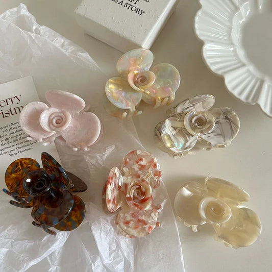 A collection of six floral-shaped acetate hair claw clips in various colors and patterns, arranged on a white surface.
