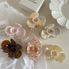 A collection of six floral-shaped acetate hair claw clips in various colors and patterns, arranged on a white surface.