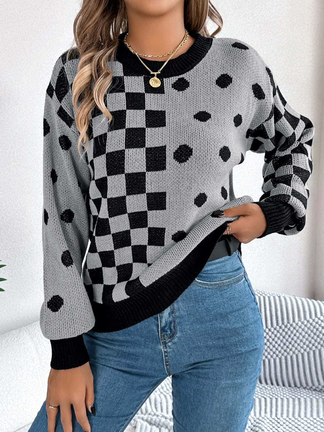 Close-up of a woman wearing a gray and black checkerboard and polka dot knit sweater and blue jeans