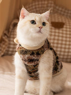 A cream-colored cat adorned in a camouflage-patterned fleece vest with a cozy texture.