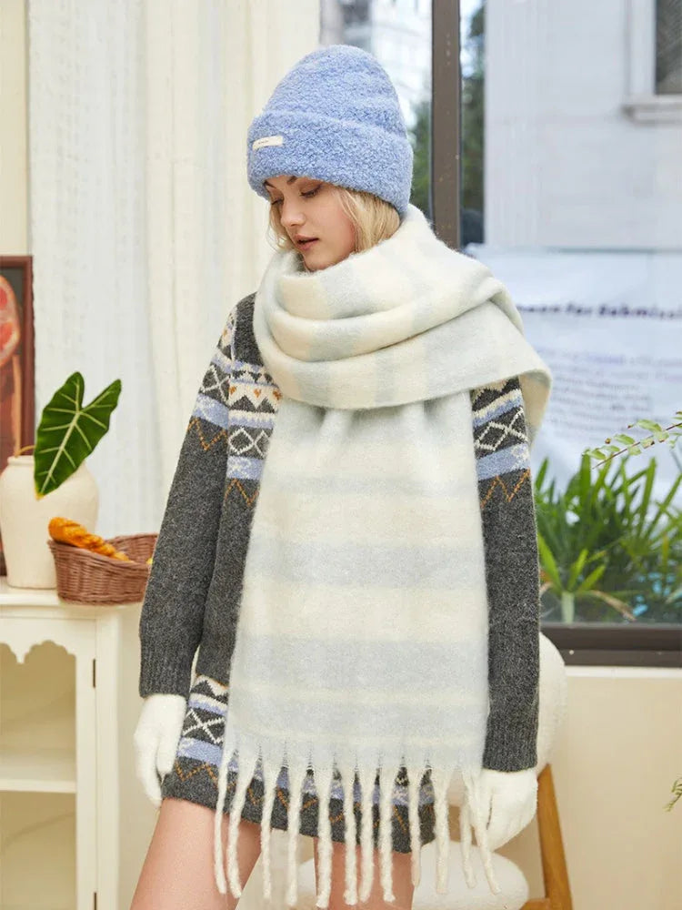 Close-up of a woman wearing a grey knit sweater with blue and white geometric pattern, a light blue beanie, and a chunky striped scarf.