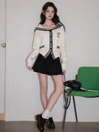 Woman wearing a white knit cardigan with black trim, styled with a black skirt and necklace.