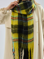 Detail shot of the fringe on a yellow and black plaid scarf worn by a woman.