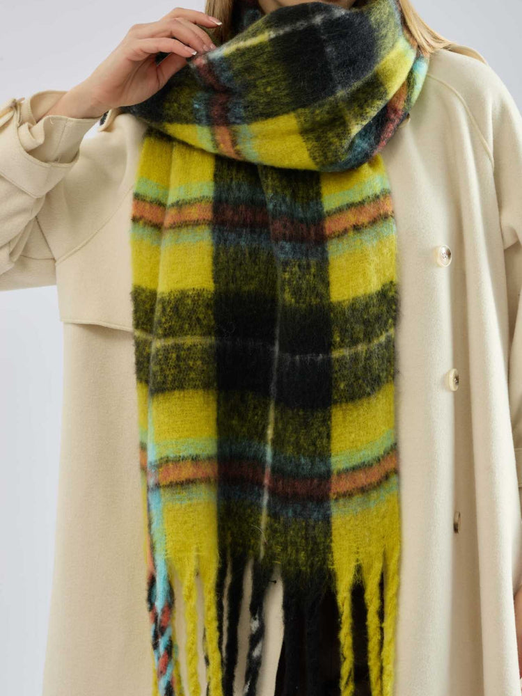 Detail shot of the fringe on a yellow and black plaid scarf worn by a woman.