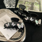 Overhead view of black claw clips with iridescent butterfly embellishments on a silver tray with various decorative elements