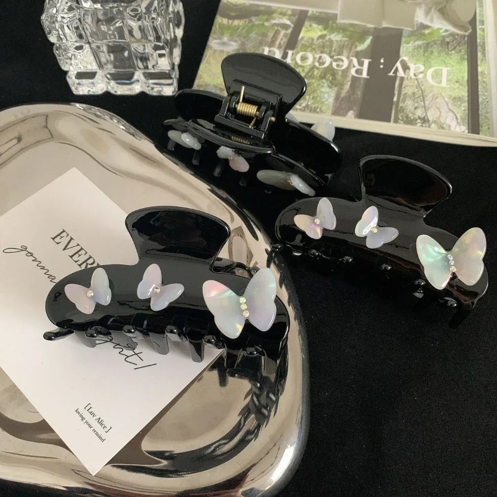 Overhead view of black claw clips with iridescent butterfly embellishments on a silver tray with various decorative elements