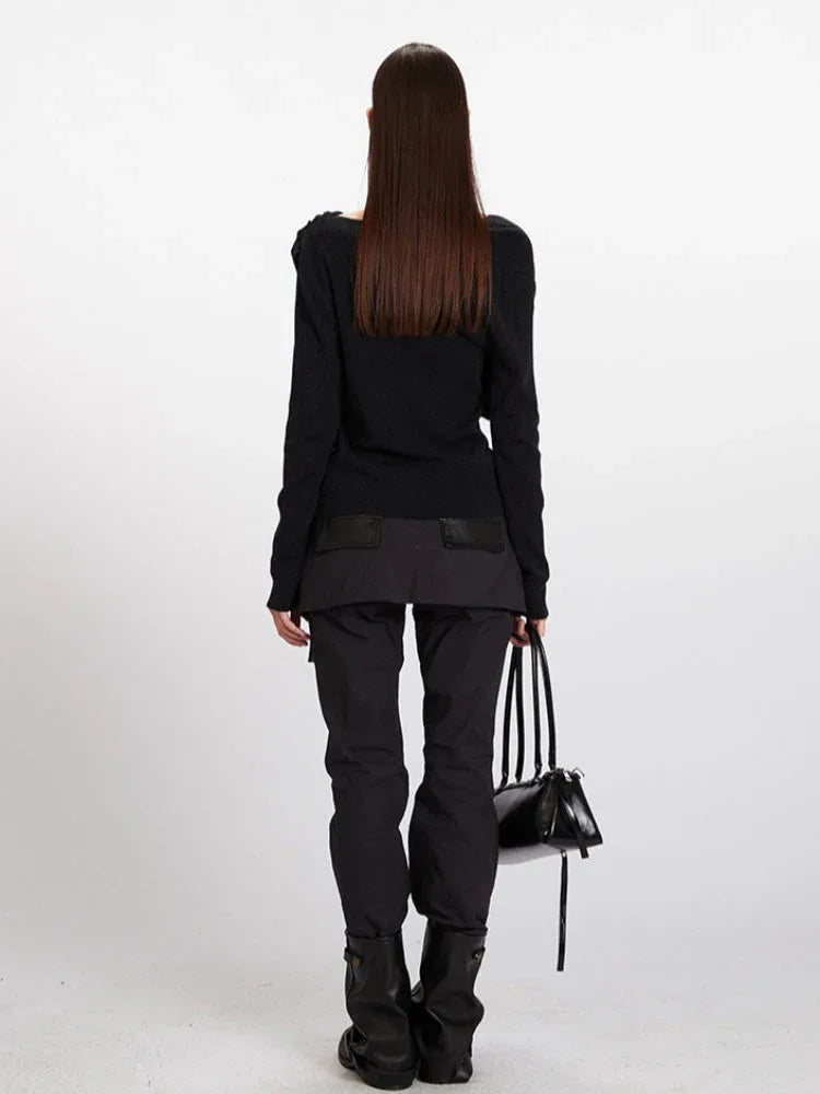 Back view of a woman wearing a black asymmetrical knit sweater and black cargo pants.