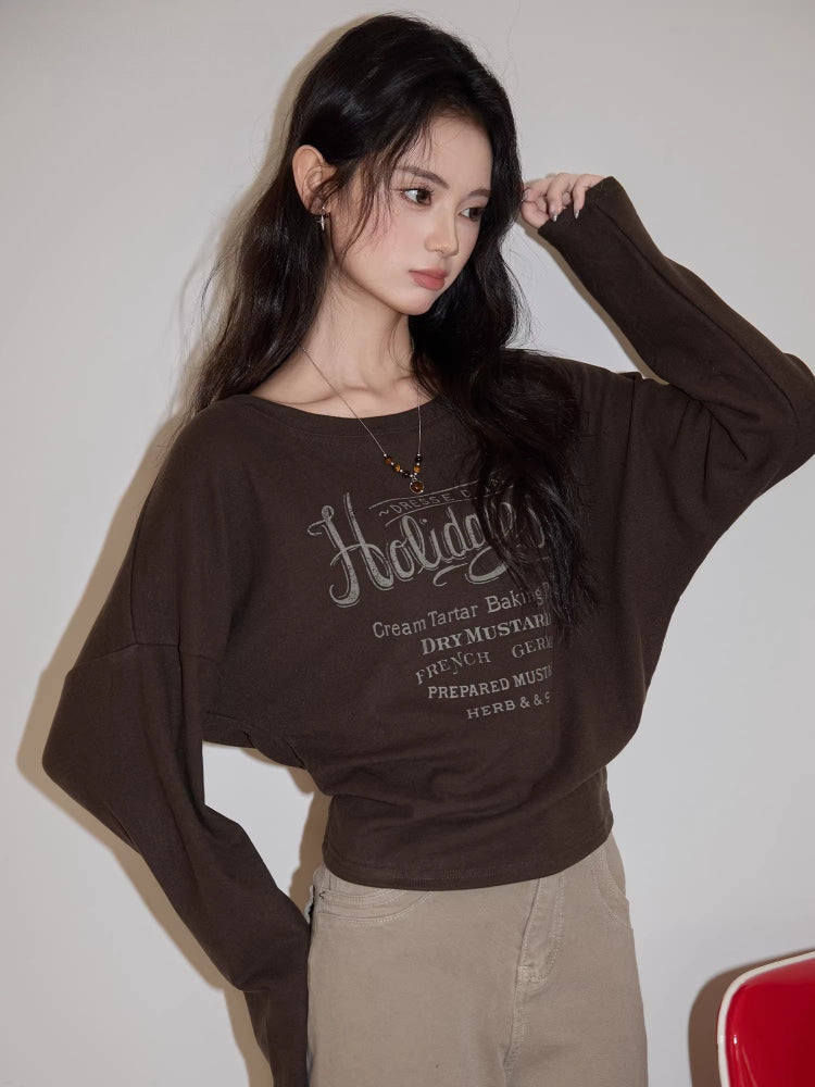 Woman wearing a brown long-sleeved graphic t-shirt and beige pants, indoors.