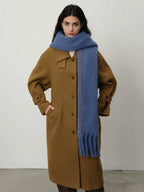 Full-body shot of a woman in a brown coat and a blue scarf